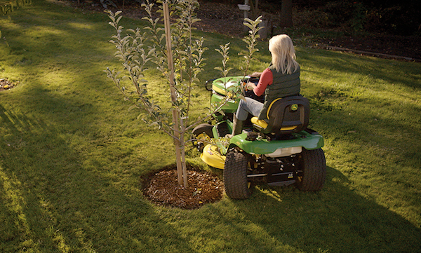 <img src=“4-Wheel-Steering-Image.jpg” alt=“Blonde woman cutting lawn with John Deere riding mower next to tree”>