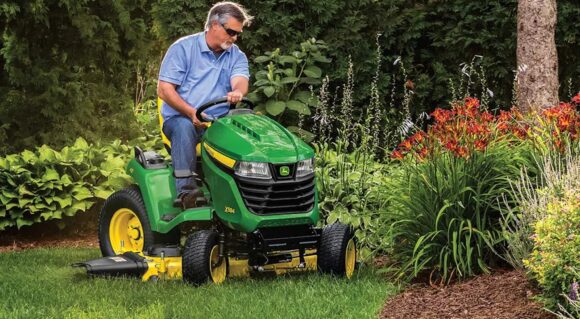 John Deere X584 lawn tractor mowing landscaped yard with mower deck