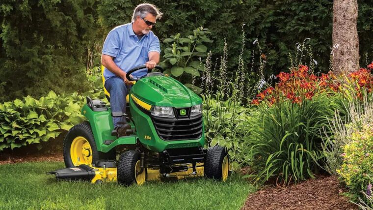 John Deere X584 lawn tractor mowing landscaped yard with mower deck