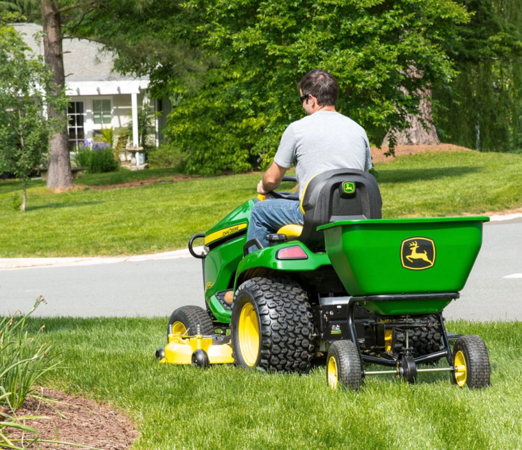 John Deere lawn tractor towing broadcast spreader across yard
