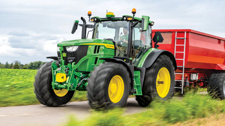 John Deere 6R row crop tractor pulling a grain cart along a farm road.