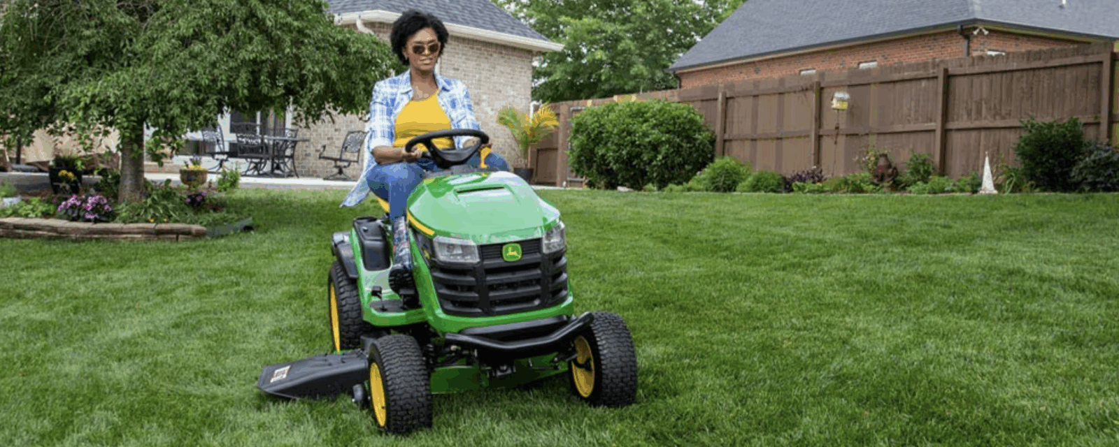 Woman riding John Deere lawn mower on her front lawn