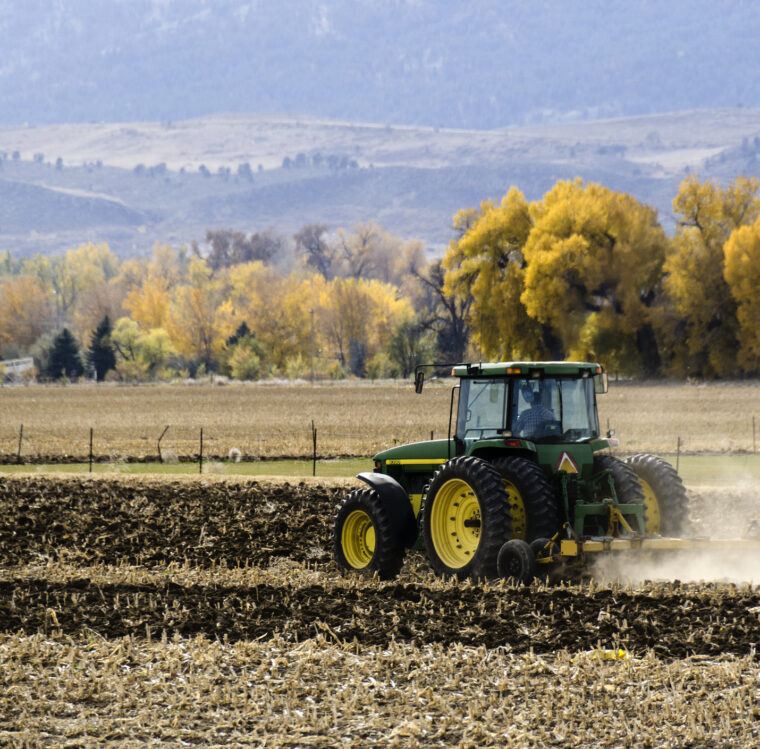 Fort Collins, Colorado, USA - October 20, 2012: A farmer in a tractor plowing a field in autumn outside of Fort Collins, Colorado, with Rocky Mountains in the background.