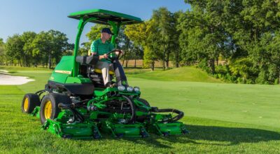 John Deere rough, trim, and surrounds mower cutting turf beside a golf course green.