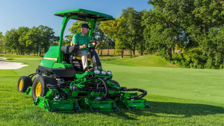 John Deere rough, trim, and surrounds mower cutting turf beside a golf course green.