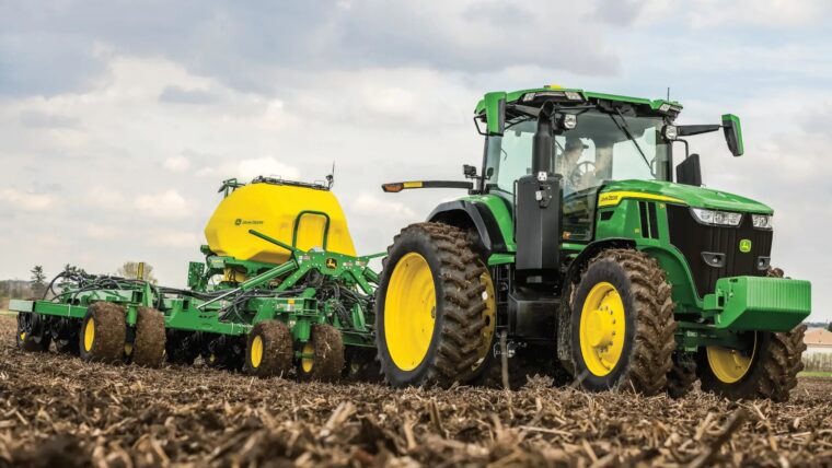 John Deere 7R row crop tractor pulling planting equipment through a field.