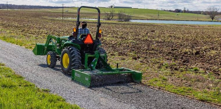John Deere tractor using a box blade to grade and smooth a gravel driveway.